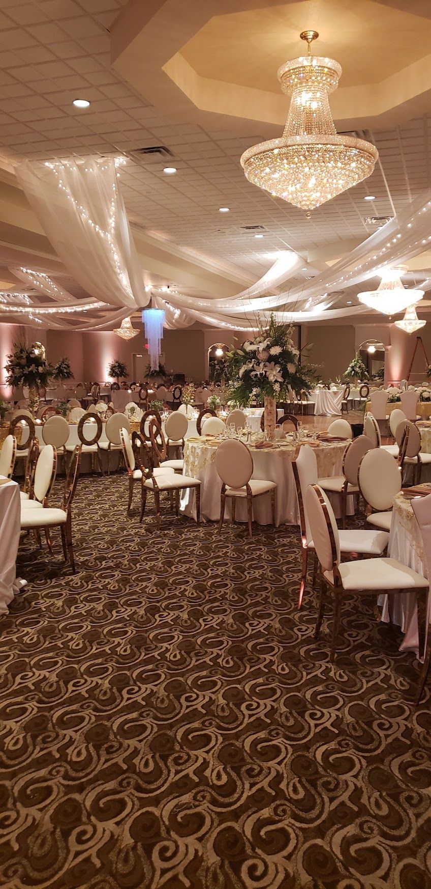 Elegant banquet hall with chandeliers, round tables, and floral centerpieces set for an event