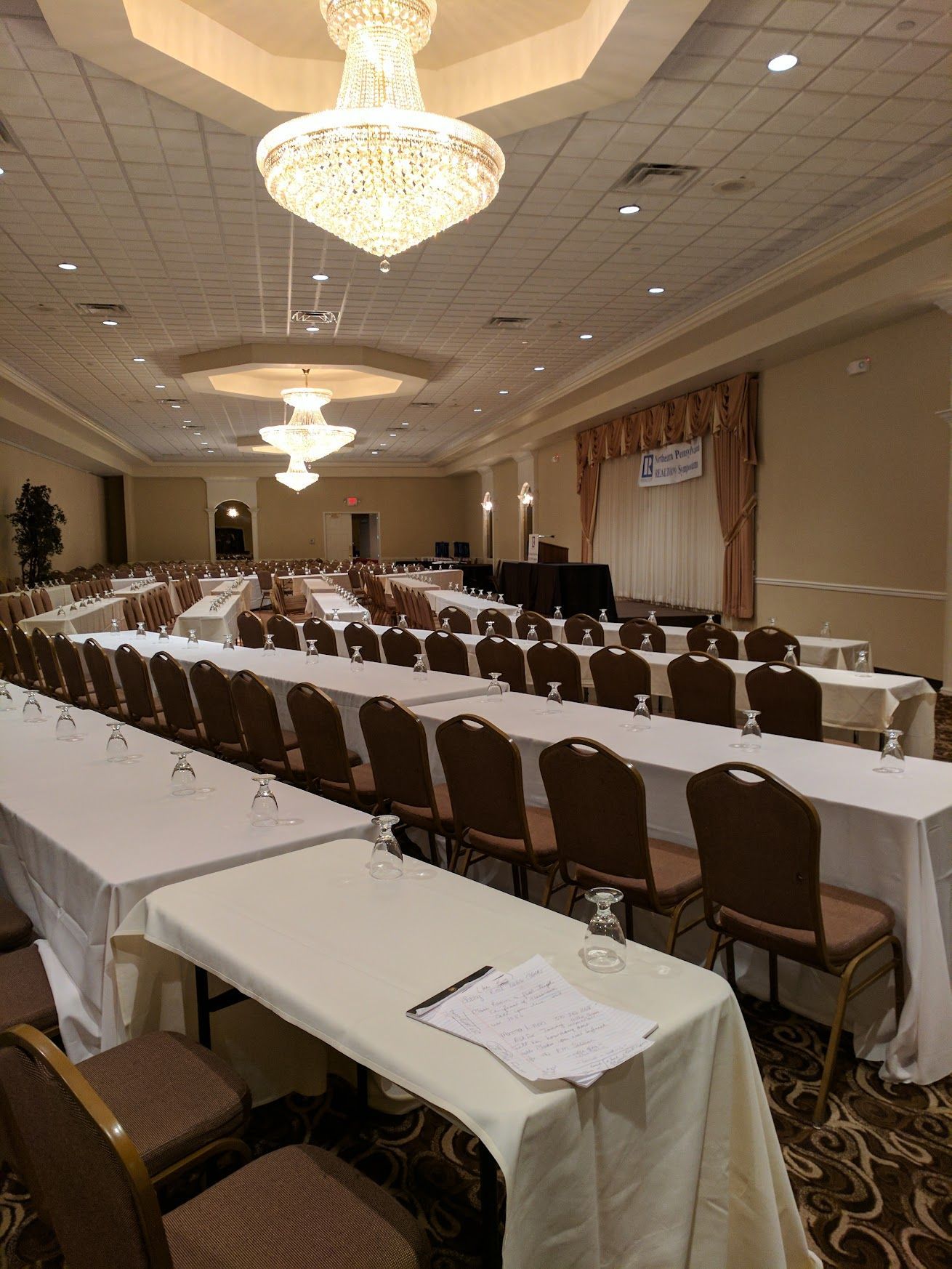 Banquet hall with U-shaped rows of tables and chairs under chandeliers, set for a meeting or conference