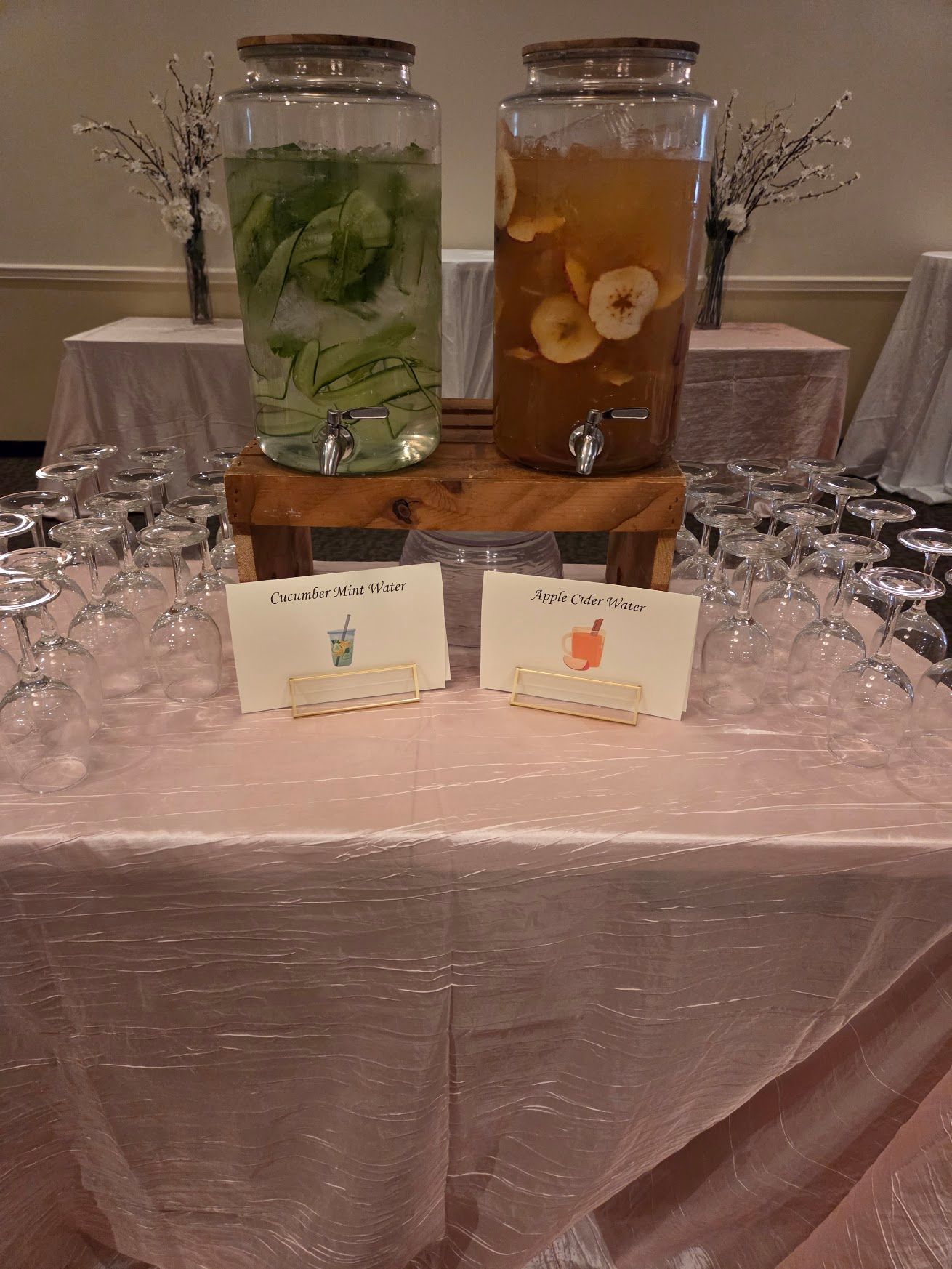 Two beverage dispensers on a pink-draped table with cups and small labels at an event