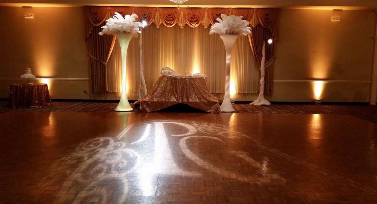 Elegant banquet hall with a decorated wedding stage, warm lights, and white floral arrangements on columns
