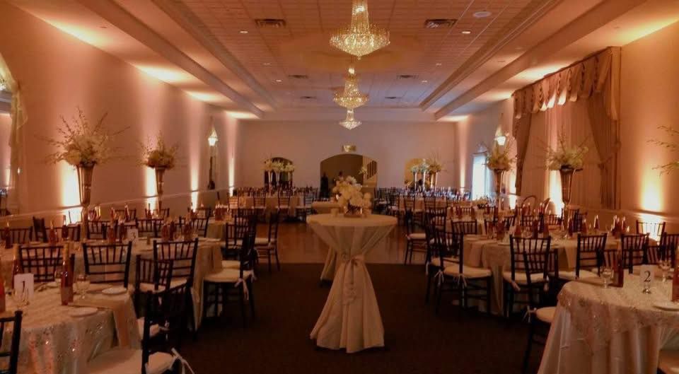 Elegant banquet hall with round tables, gold chairs, chandeliers, and warm pink lighting