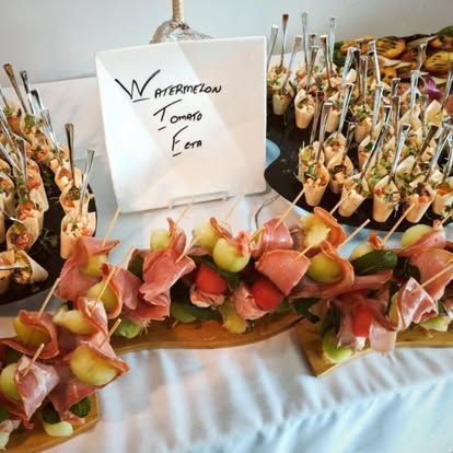 Watermelon and tomato feta appetizers on a buffet tray with a handwritten label.