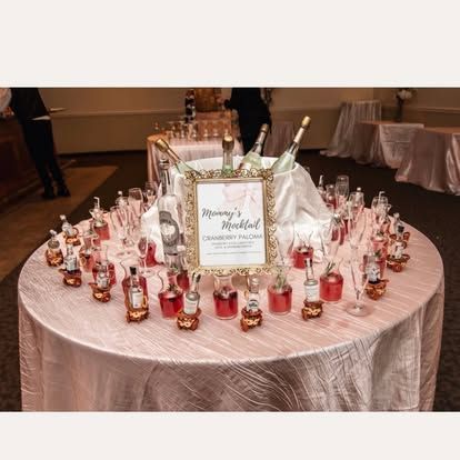 Round table with pink glass vases and a framed wedding sign at a reception.