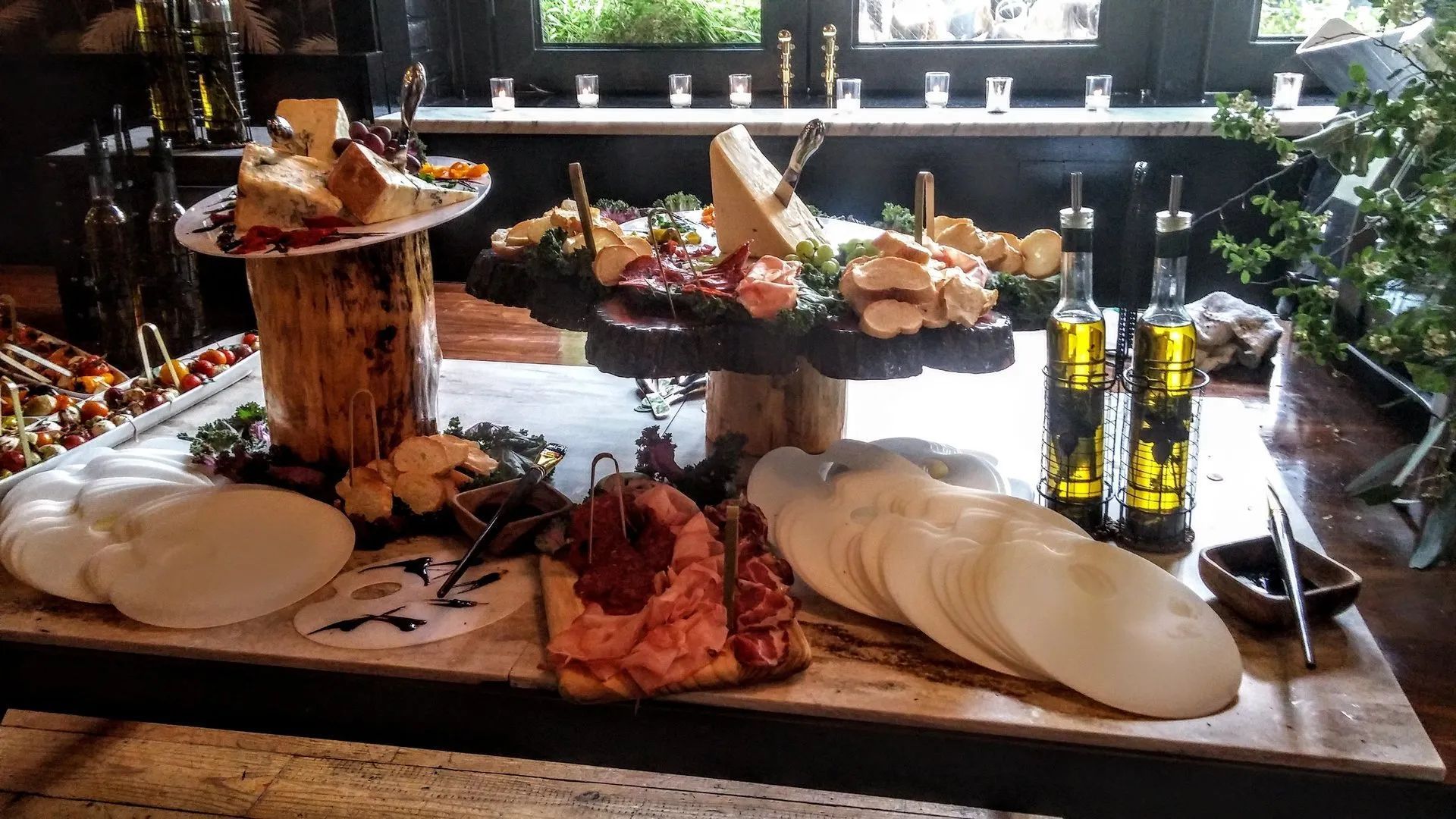 Buffet spread with plated appetizers, breads, olives, and olive oil bottles on a wooden table
