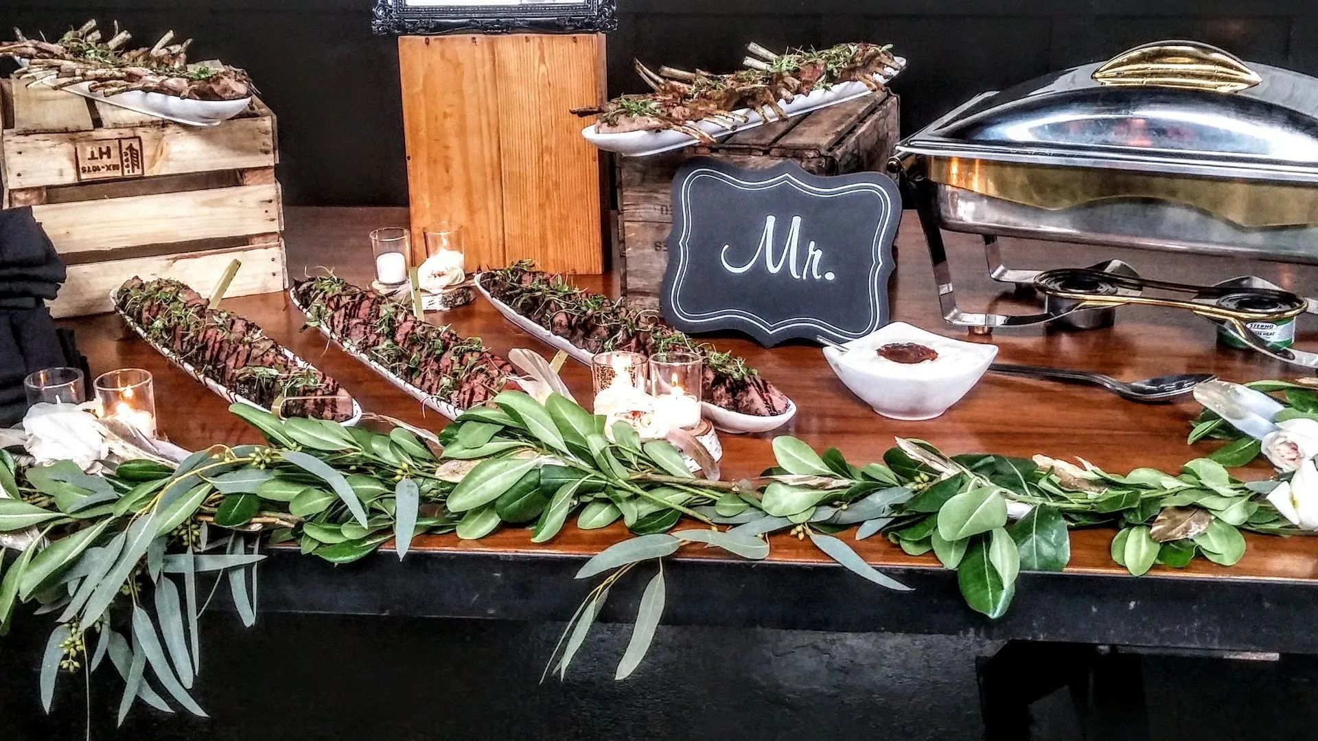 Dessert buffet with pies, pastries, green foliage, and a chalkboard sign on a wooden table