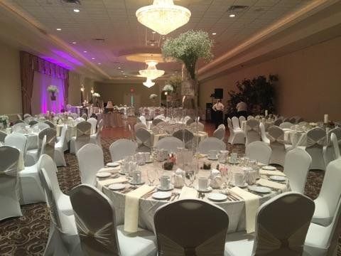 Elegant banquet hall with round white-clothed tables, chiavari chairs, and purple uplighting