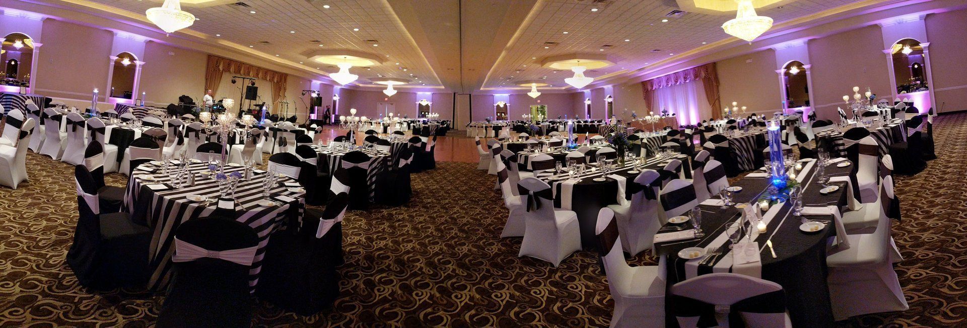 Banquet hall with round tables, white chairs, and purple lighting set for an event