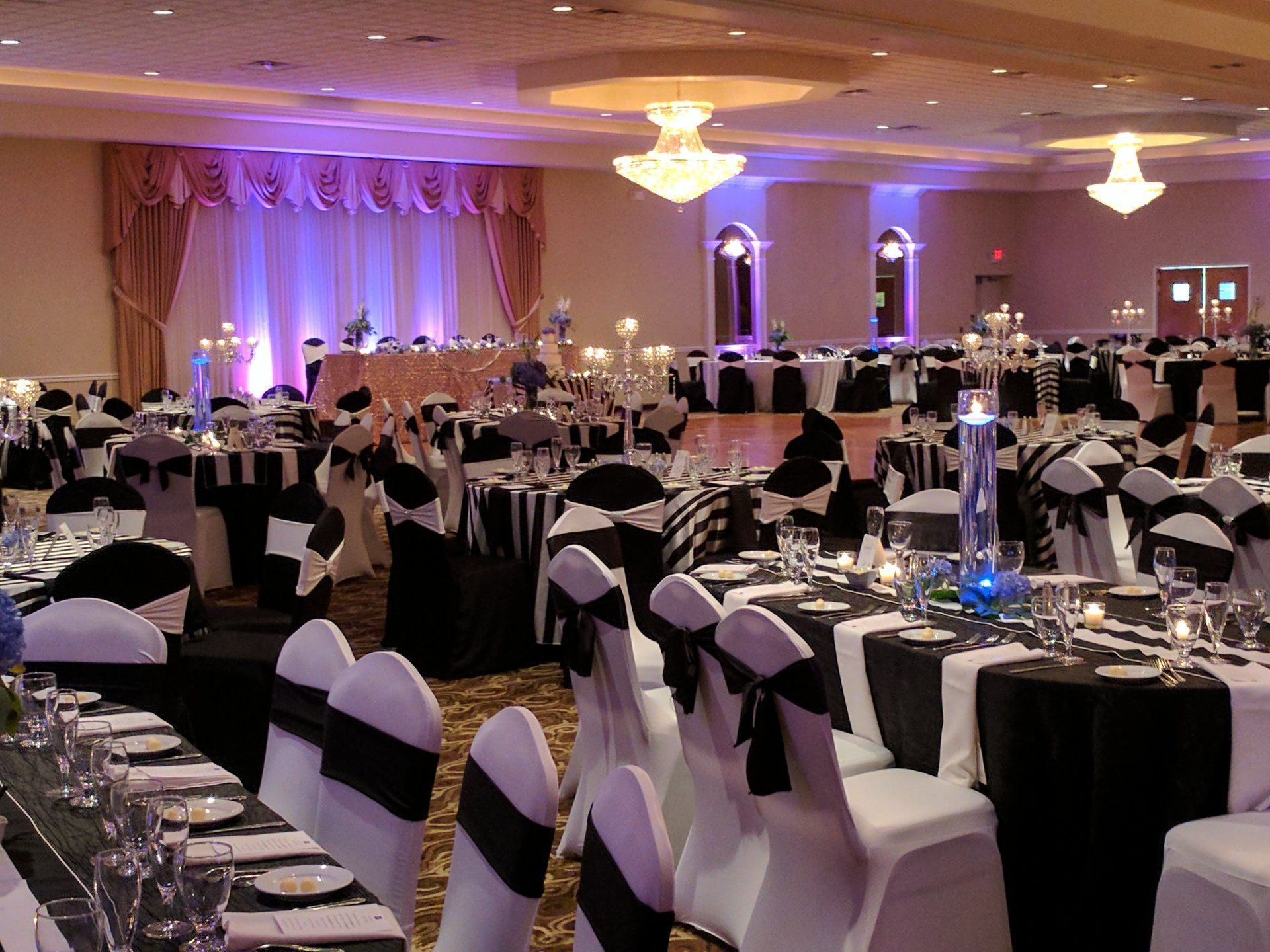 Decorated banquet hall with round tables, black chair covers, and purple uplighting before an event