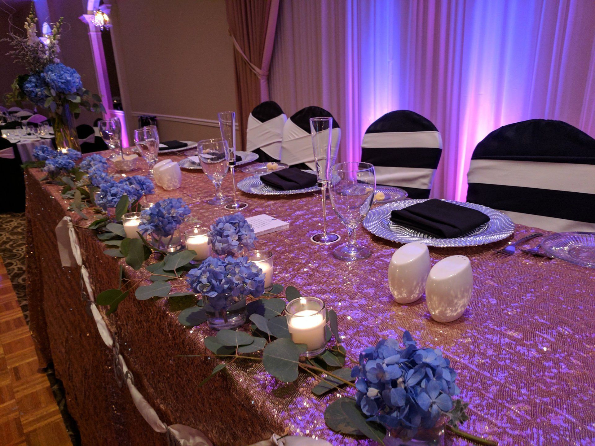Elegant banquet table with purple lighting, white chairs, candles, and blue floral centerpieces