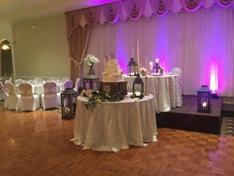 Decorated banquet hall with dessert tables, white drapes, and purple uplighting on a parquet floor