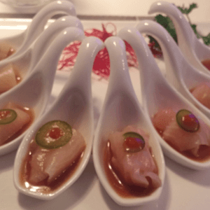 White spoon display with pale dessert topped by green and red fruit slices on a table