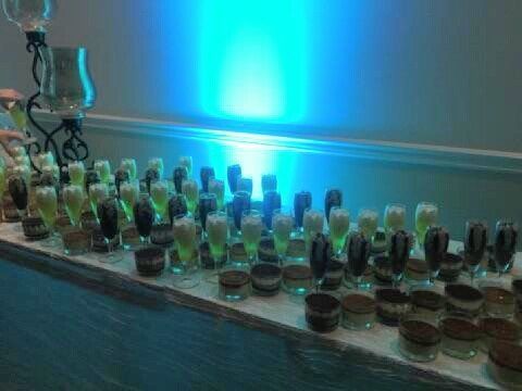Rows of small glass bottles and bowls on a table, lit by blue light against a wall.
