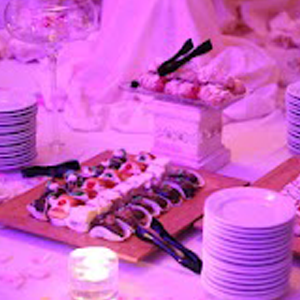 Pink-lit buffet table with stacks of plates and trays of assorted desserts and pastries