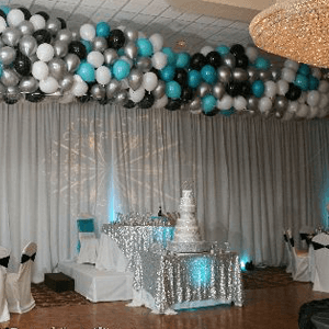Elegant event room with silver, black, and turquoise balloon garland, draped curtains, and decorated tables