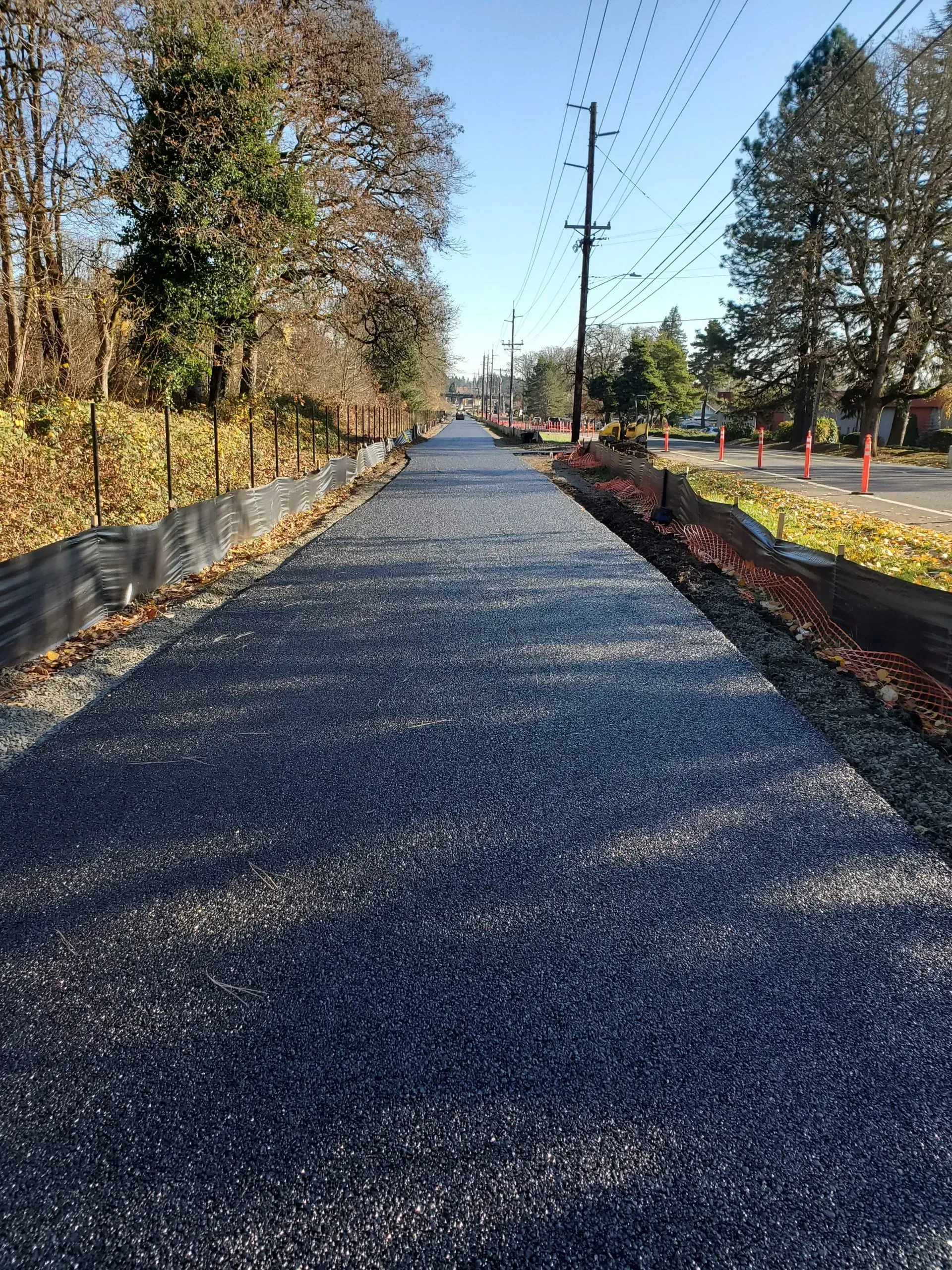 Gravel road under construction beside trees, utility poles, and orange cones on a sunny day