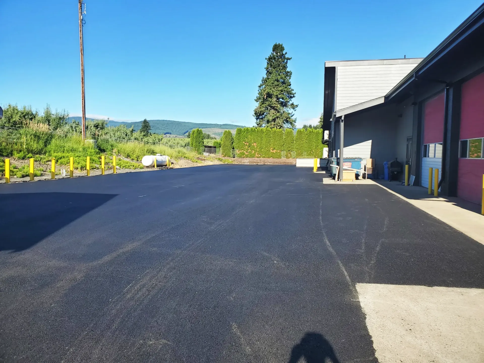 A freshly paved asphalt parking lot next to a commercial building under a clear blue sky.