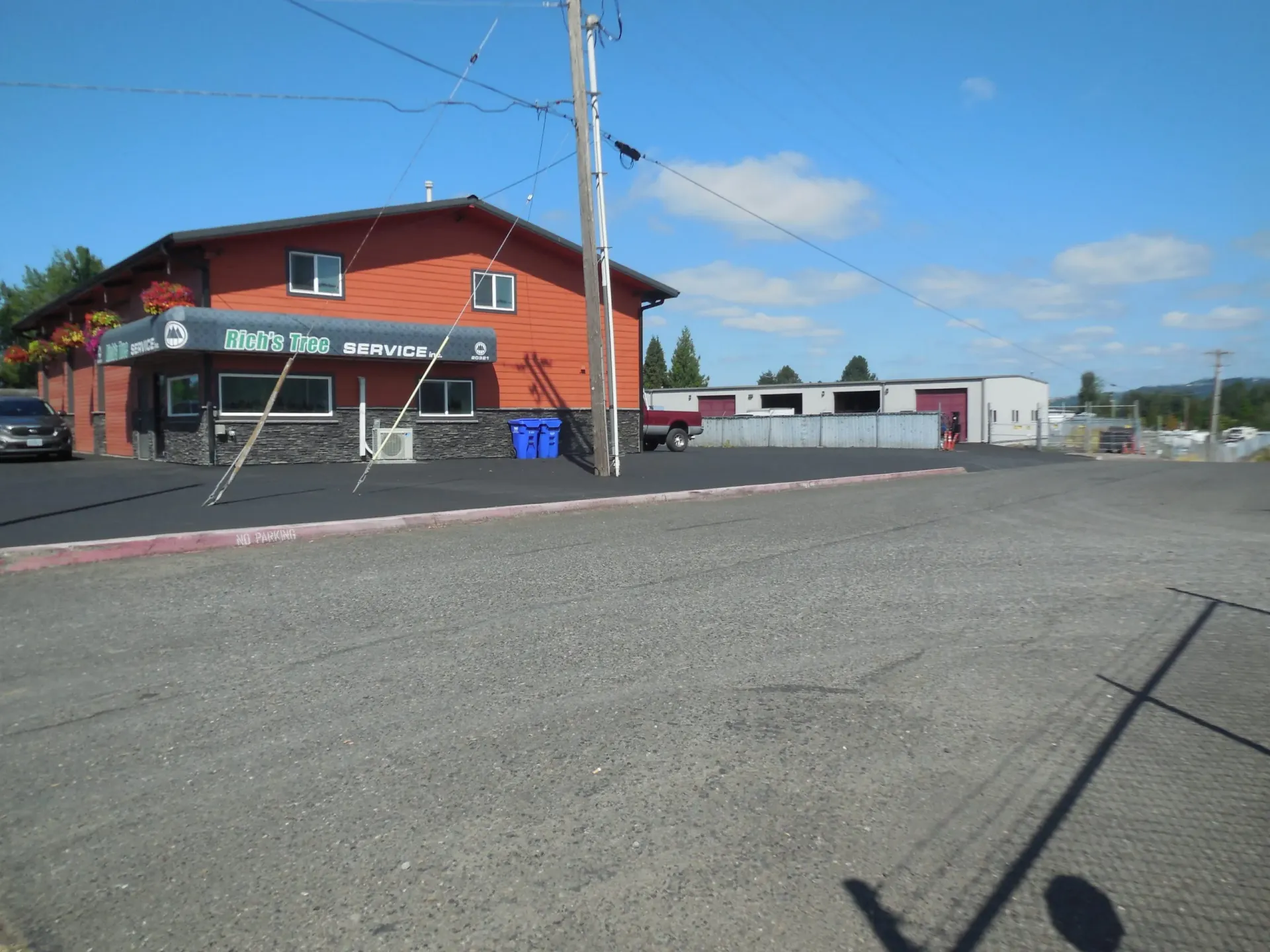 A red building with a storefront entrance and a gravel parking lot under a clear blue sky.