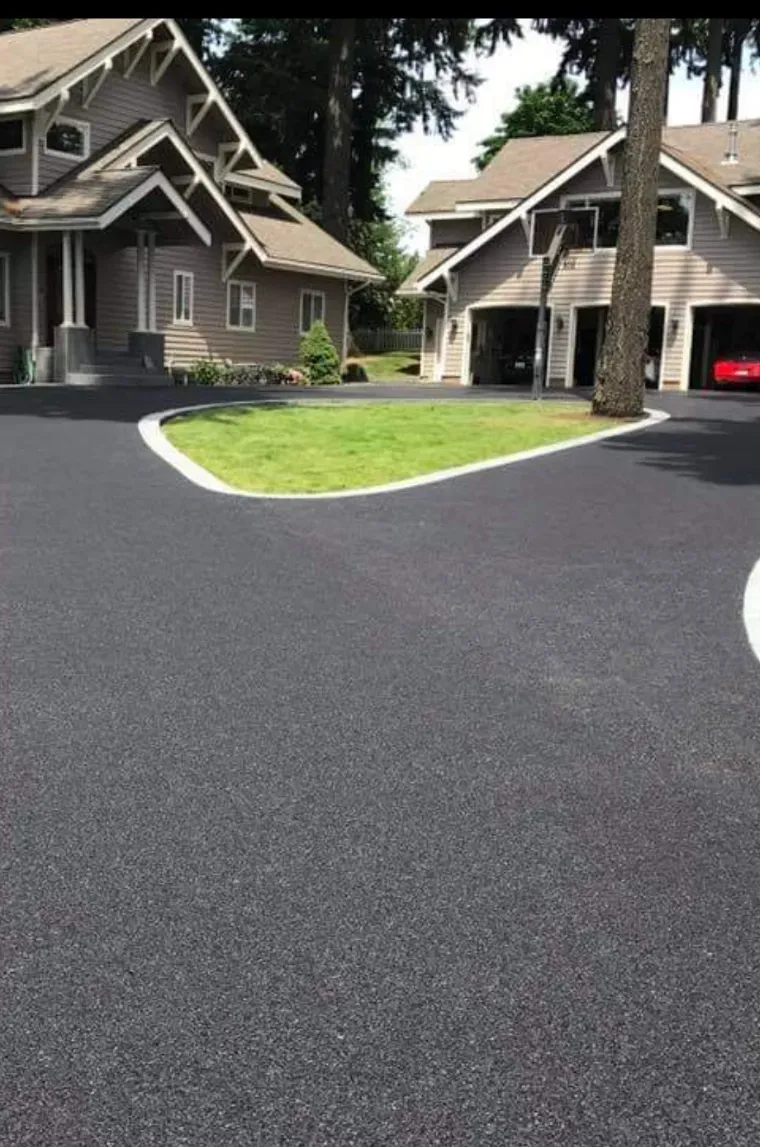A paved driveway leading to two large, shingled houses with a grass-covered island in the center.