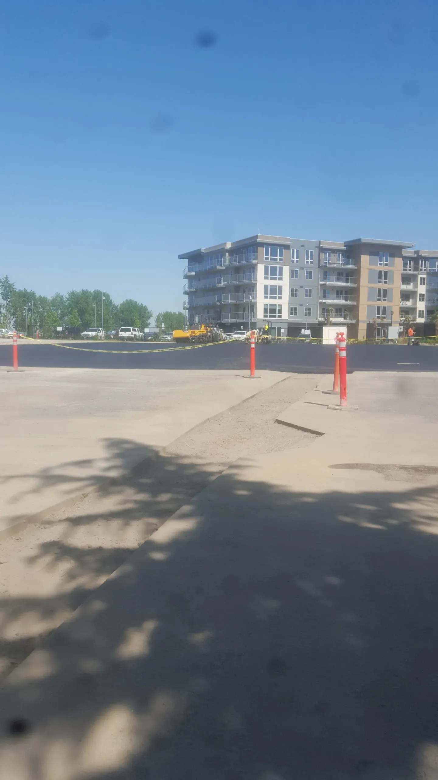 A paved area with orange safety bollards leads toward a multi-story apartment building under a clear blue sky.