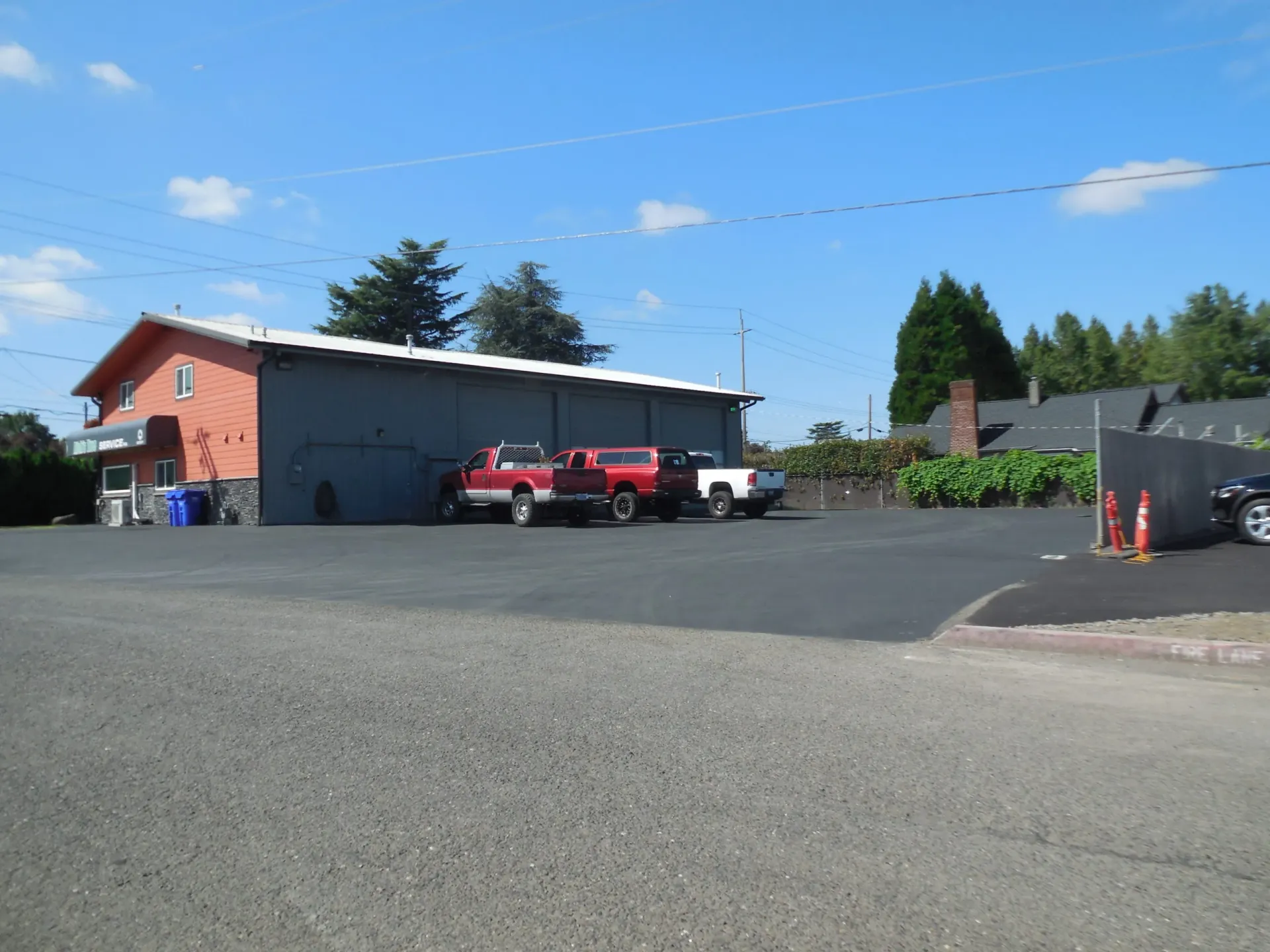A red and grey commercial building with a paved parking lot containing three parked pickup trucks under a blue sky.