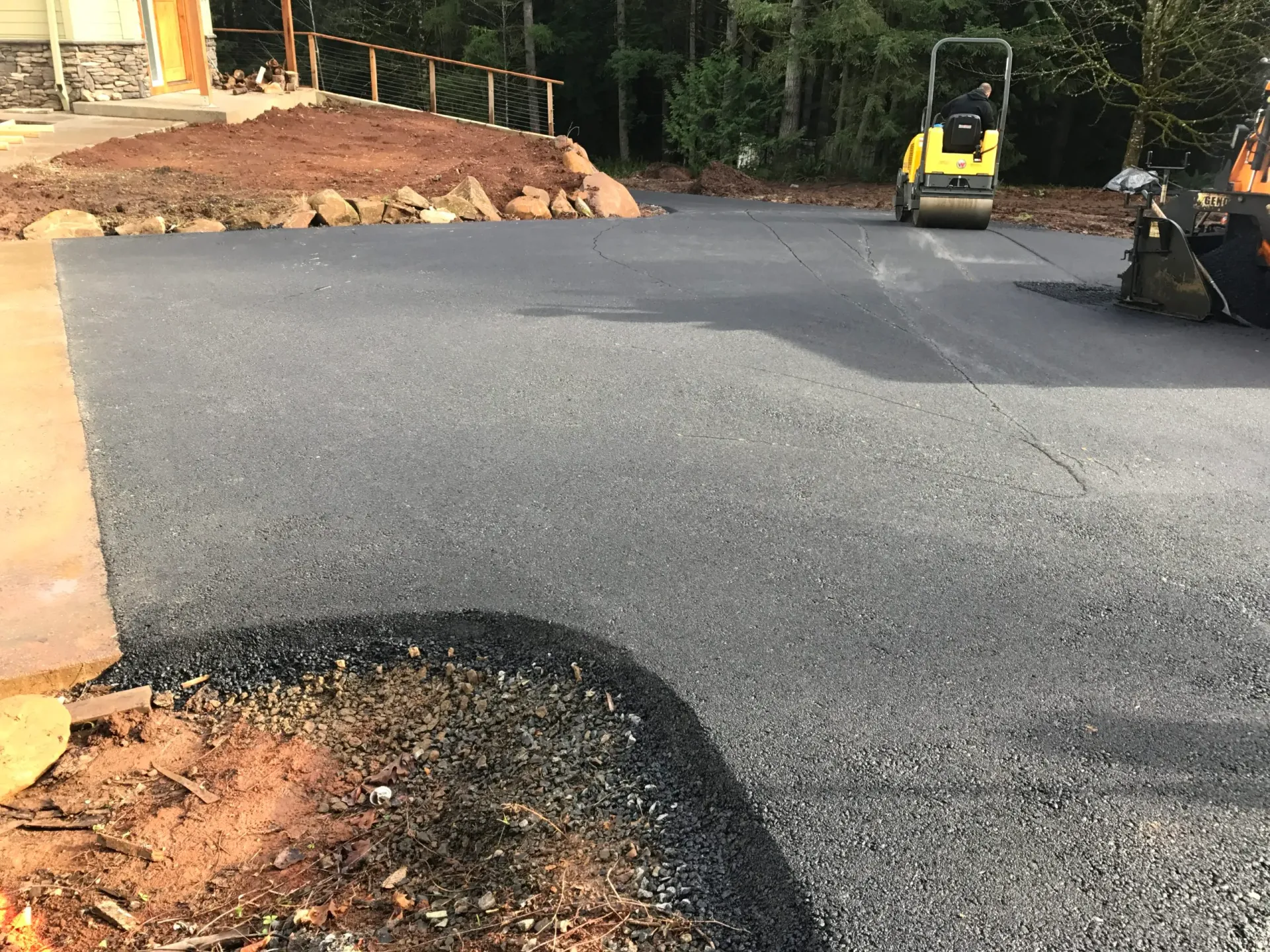 A freshly paved asphalt driveway under construction with a yellow steamroller in the background.