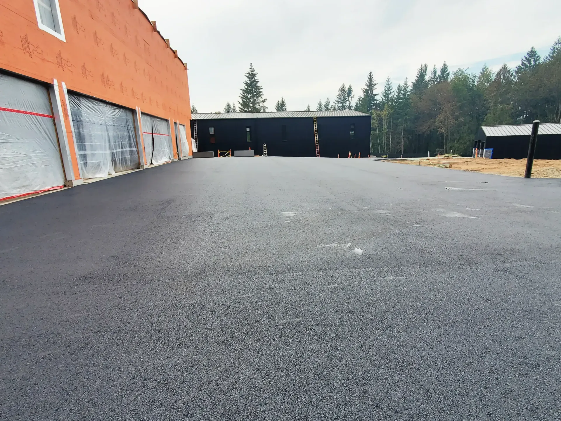 Freshly paved black asphalt driveway leading toward a modern building exterior with orange walls and dark siding.