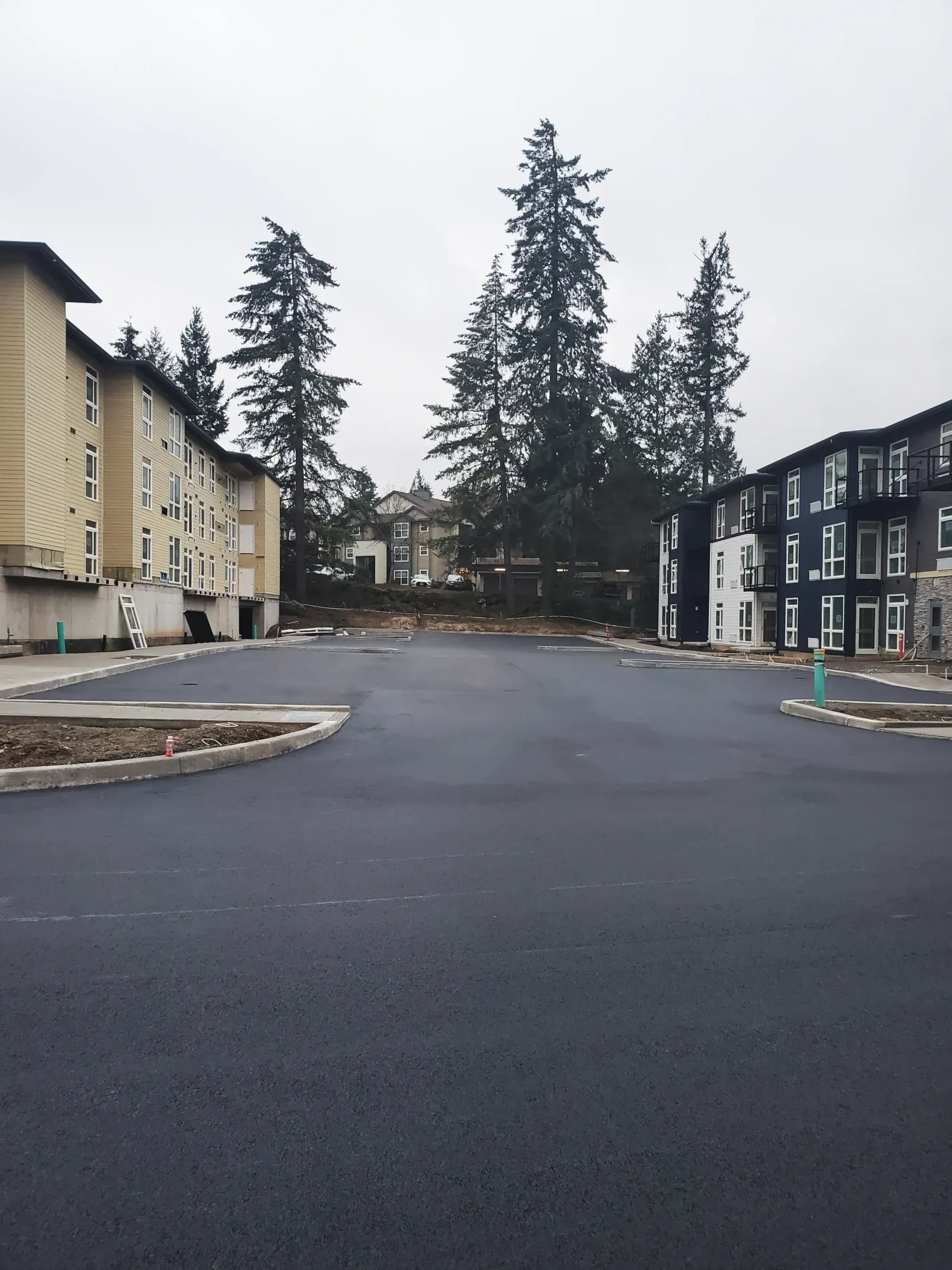 A freshly paved, empty parking lot between a beige building on the left and a dark-colored building on the right.