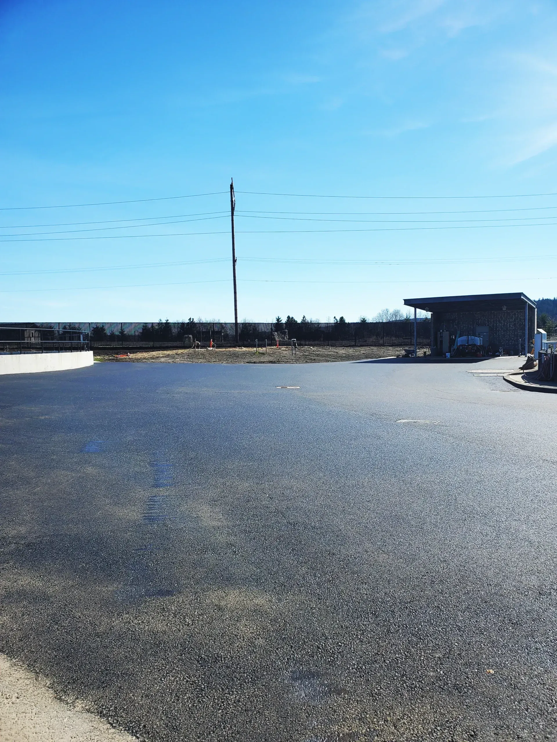 A large asphalt parking lot under a clear blue sky, with a stone-covered structure visible in the distance.