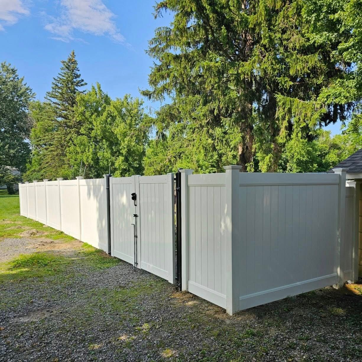 A white vinyl fence with a gate and trees in the background.