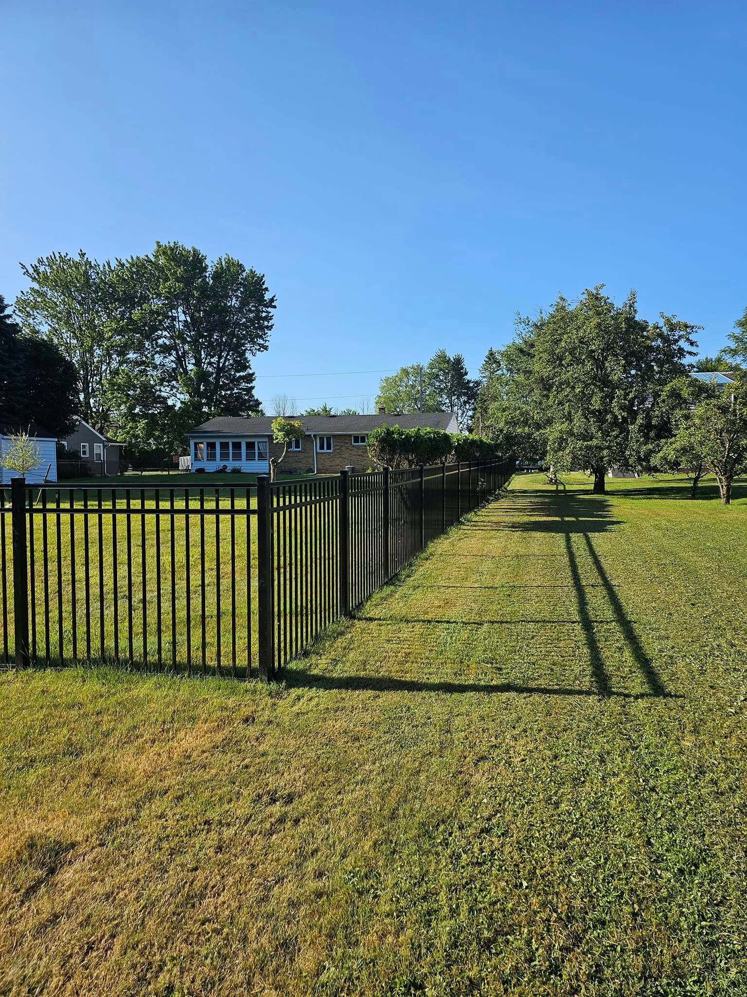 A fence surrounds a lush green field with a house in the background.