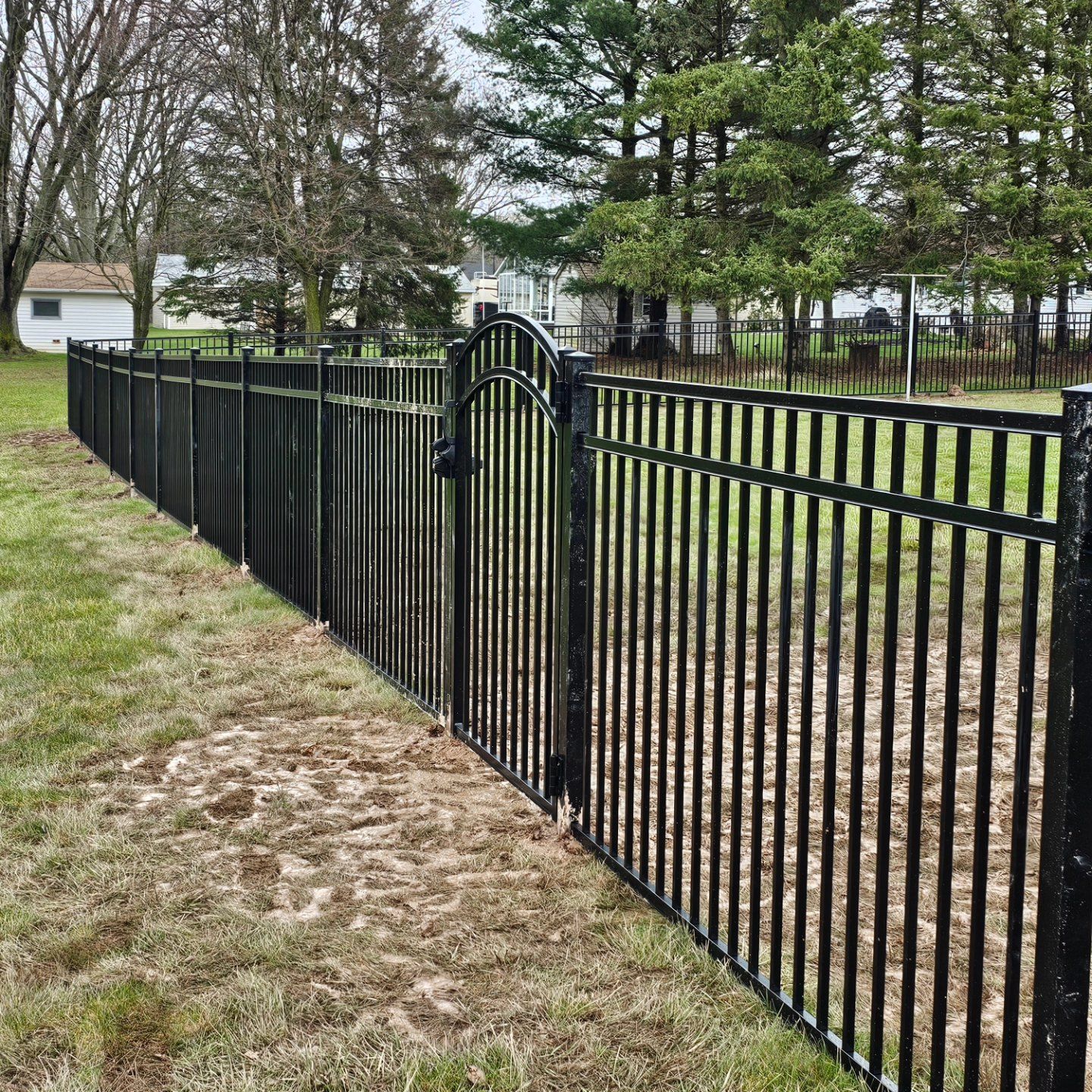 A black metal fence with a gate in the middle of a grassy field.