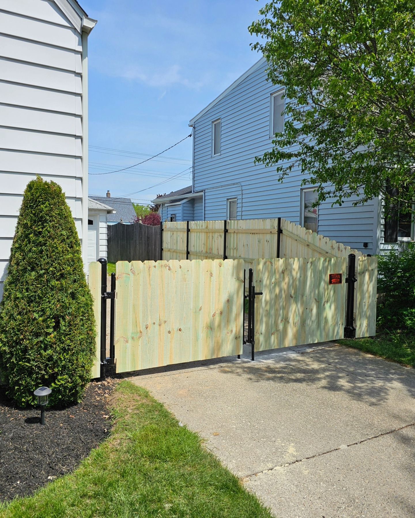 A wooden fence is surrounding a driveway in front of a house.