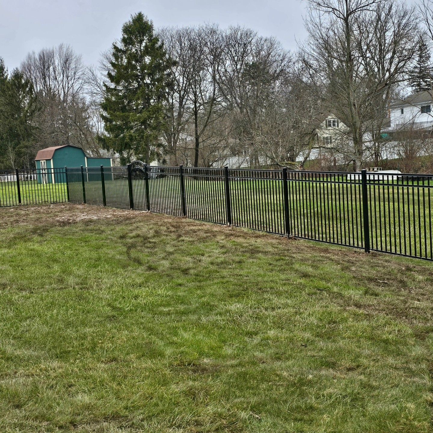 A fence surrounds a grassy field with trees in the background