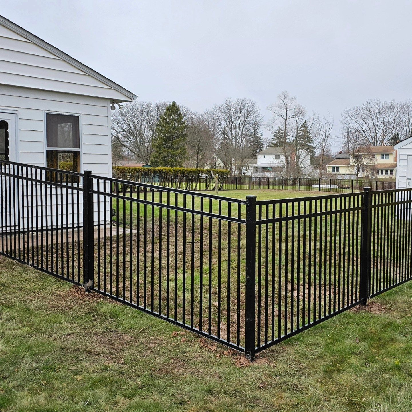 A black metal fence surrounds a grassy yard in front of a house.