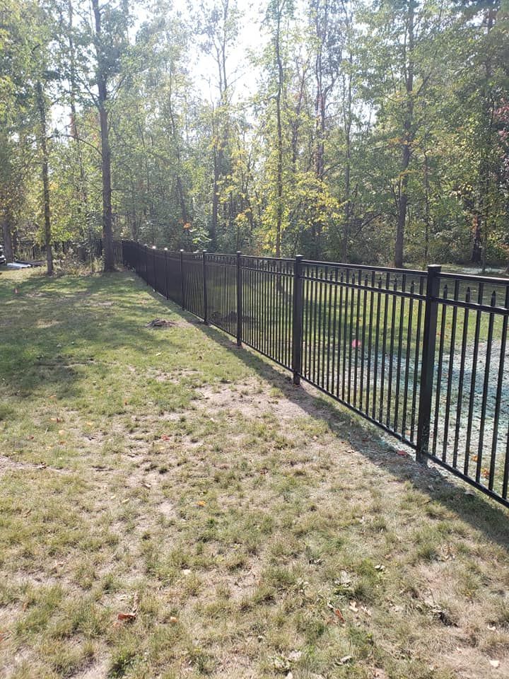 A black metal fence surrounds a lush green field.