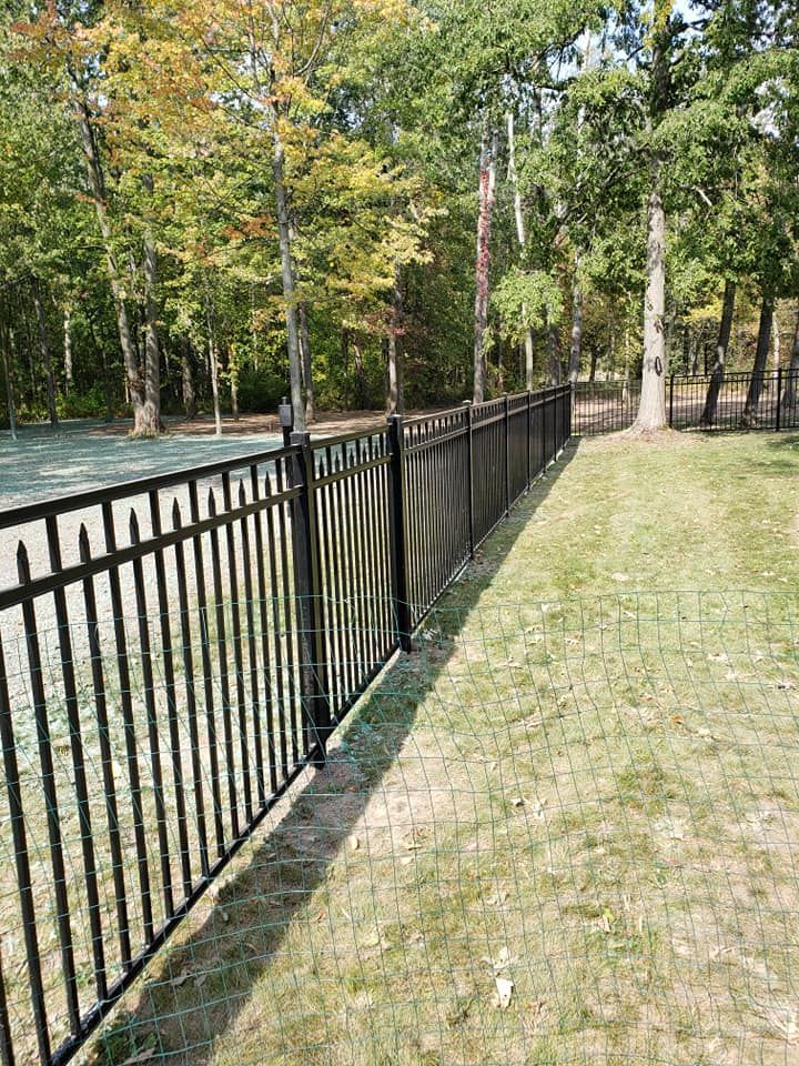 A black fence surrounds a basketball court in a park.