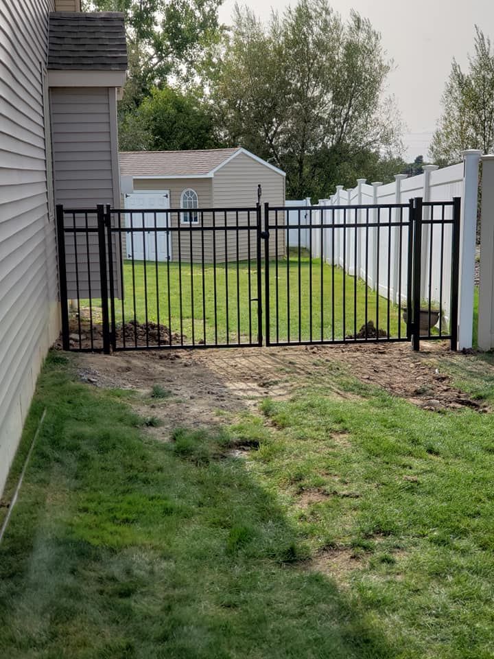 A black metal fence is surrounding a lush green yard.
