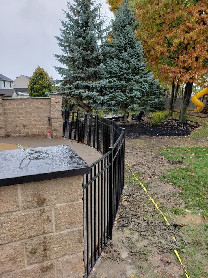 A black fence is surrounding a brick wall in a backyard.