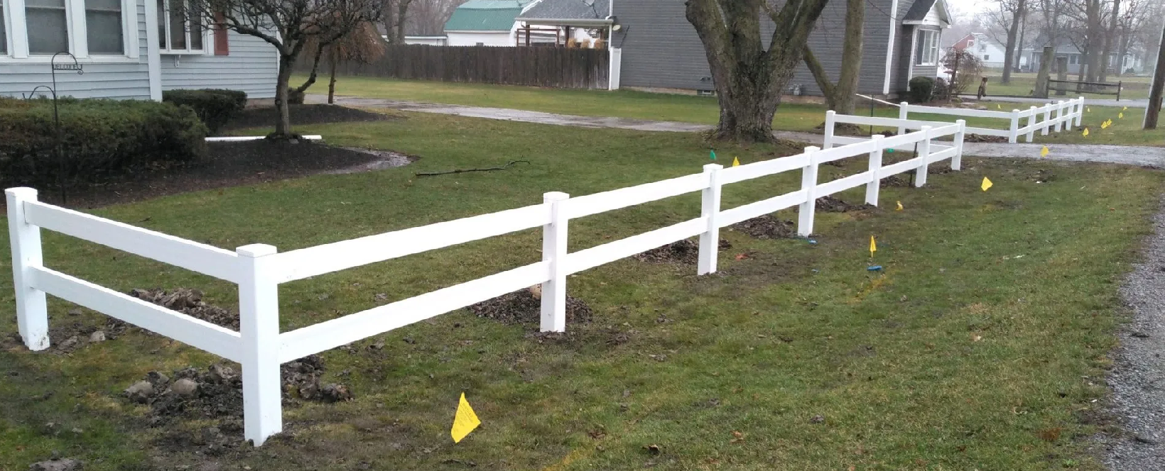 White picket fence along a grassy yard in front of houses and trees.
