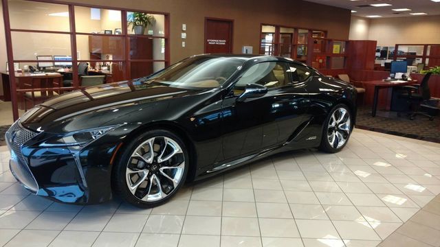 Black Lexus LC coupe displayed inside a dealership, with beige interior and shiny chrome wheels.