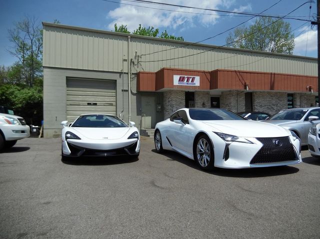 Two white cars parked outside an auto repair shop with a tan and brick exterior.