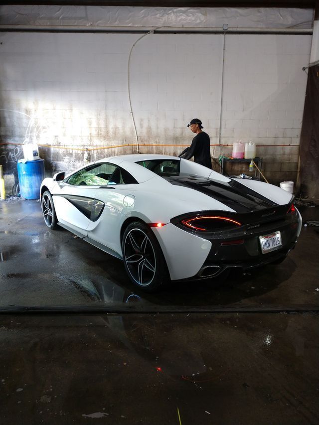 White McLaren sports car being washed in a garage; person in the background.