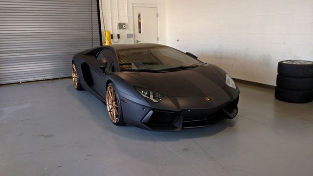 Matte black Lamborghini Aventador with bronze wheels in a garage.