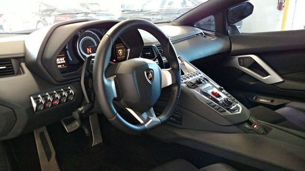 Interior view of a black Lamborghini. Dashboard and steering wheel are visible, with silver accents and buttons.