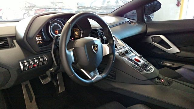 Interior view of a black Lamborghini. Dashboard and steering wheel are visible, with silver accents and buttons.