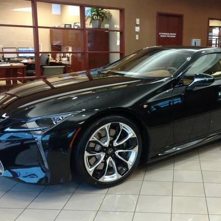 Black Lexus coupe on display in a car dealership, with shiny chrome wheels.