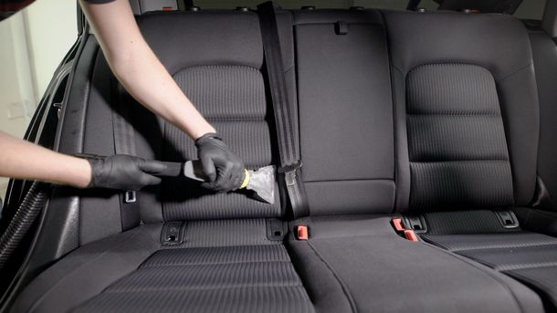Person vacuuming crumbs from a black car's back seat with a handheld nozzle