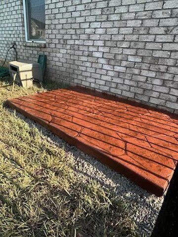 A wooden deck is sitting in the grass in front of a brick building.