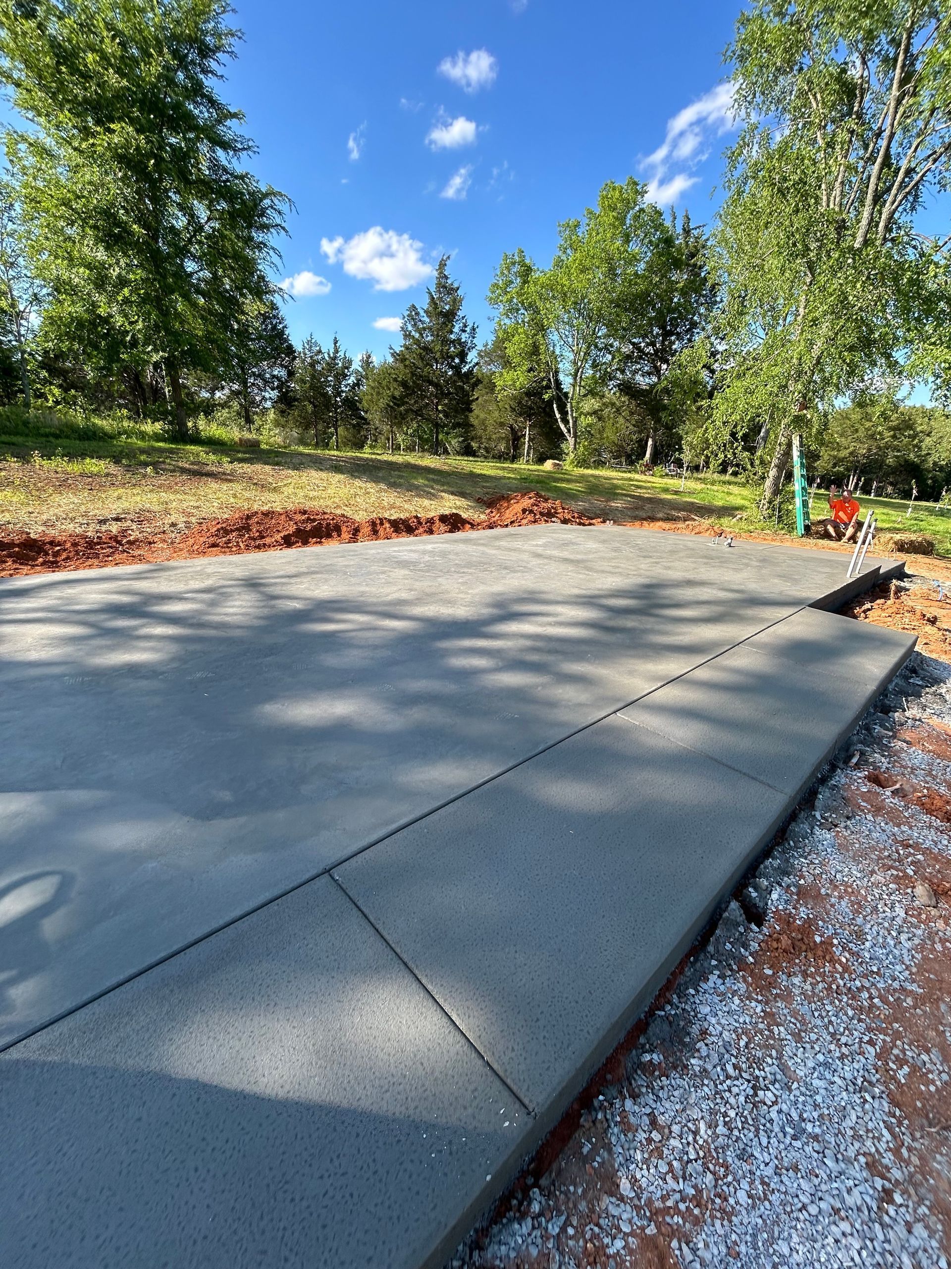 Newly poured concrete slab and curb with a green landscape background.