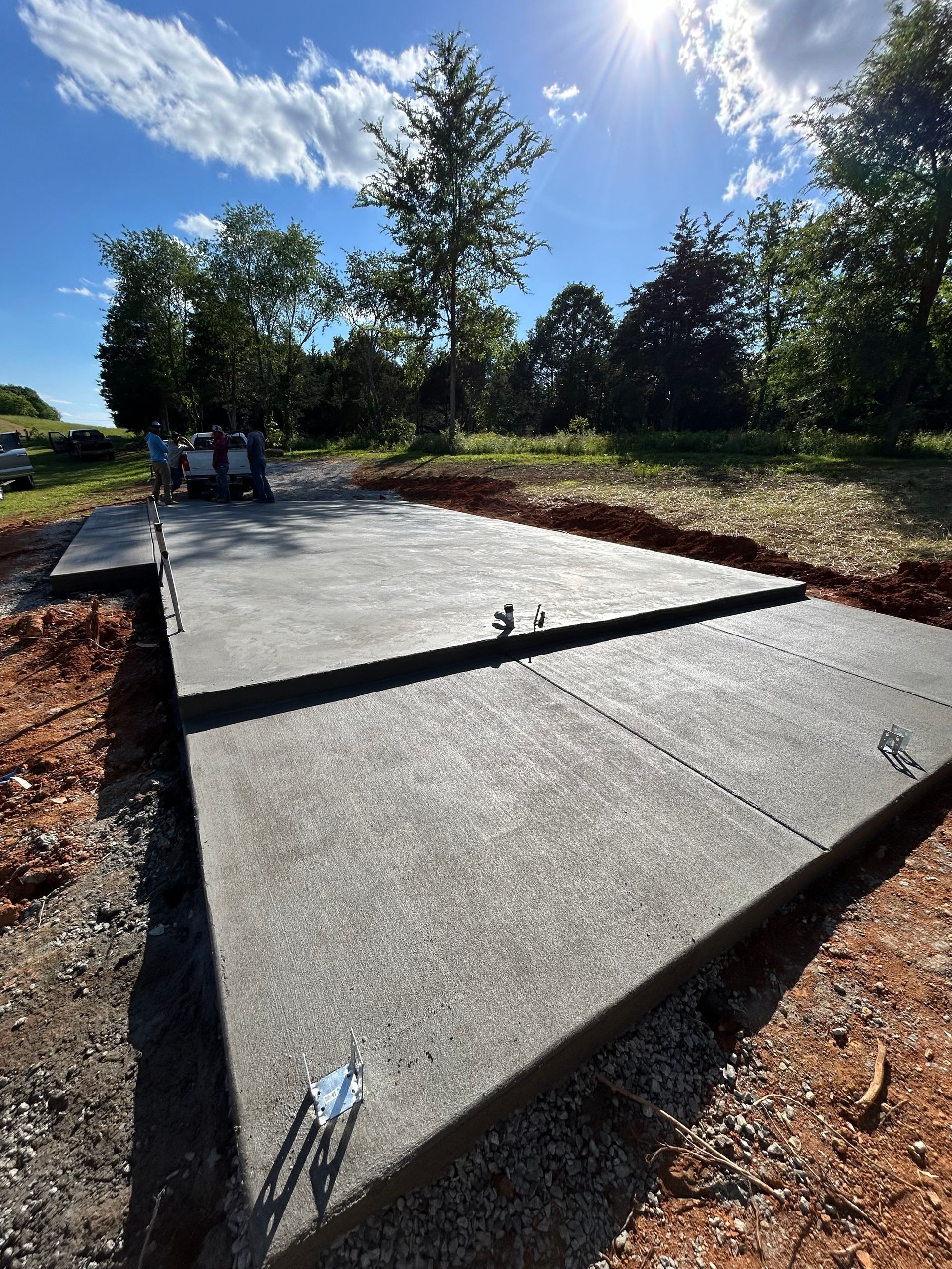 Newly poured concrete pad in an outdoor setting. Blue sky and trees in background.